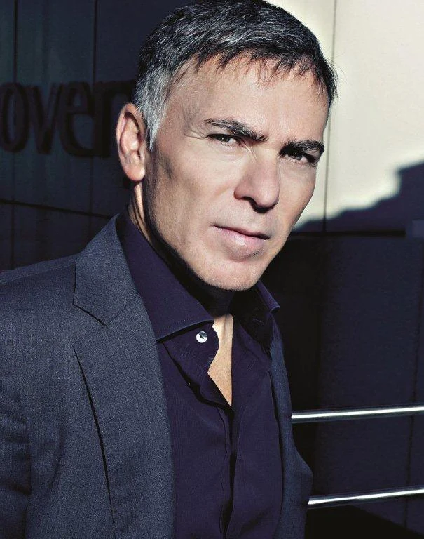 Adrian Gore in the full supplied colour portrait, wearing a dark jacket and open-neck shirt outside an office building.