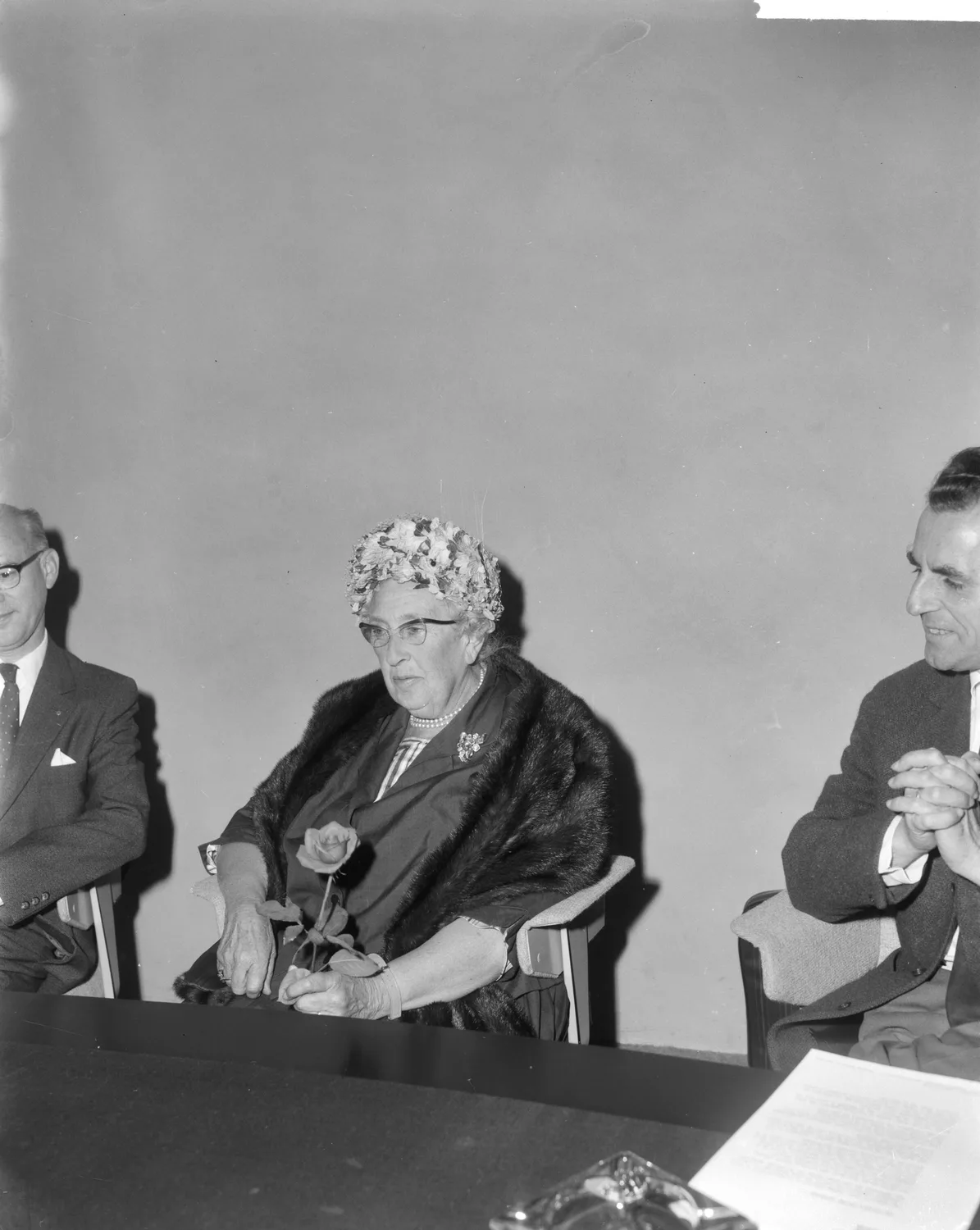Agatha Christie seated at the centre of a Schiphol Airport photograph in 1964, holding a rose, with other people and the full table retained
