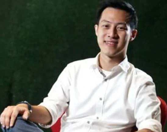 Andrew Darwis in a white shirt against a dark green background.