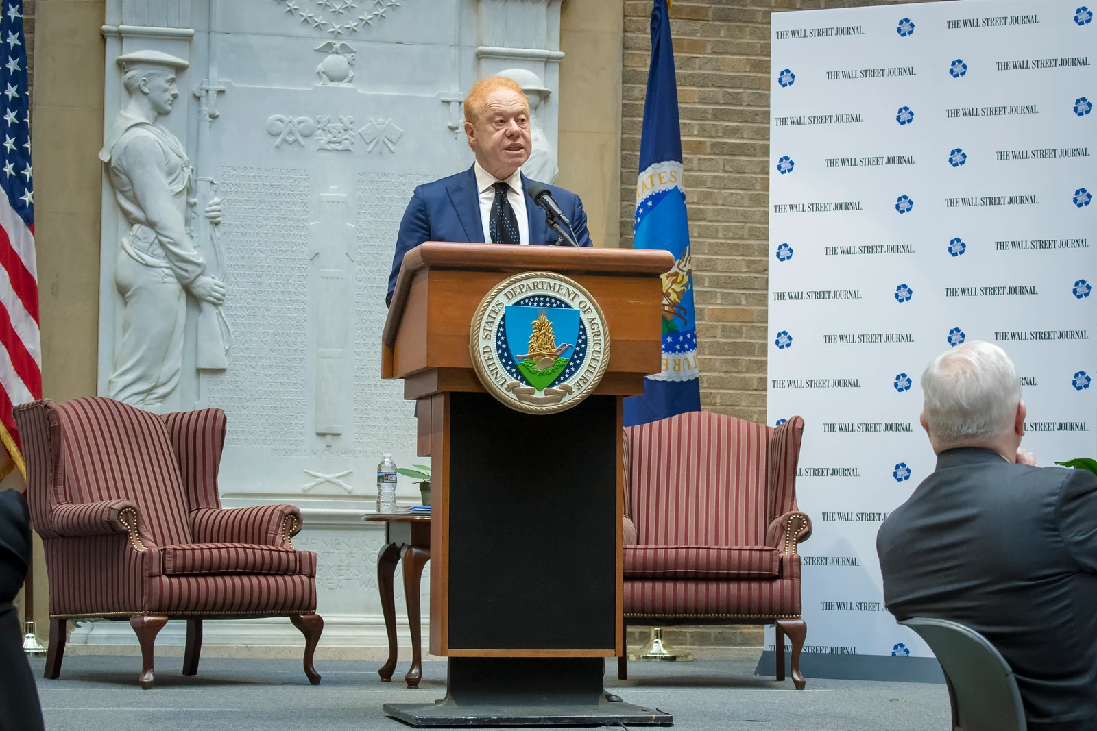 Complete USDA photograph of Anthony Pratt speaking behind a lectern in Washington in 2018, retaining the chairs, audience, flags and forum backdrop.
