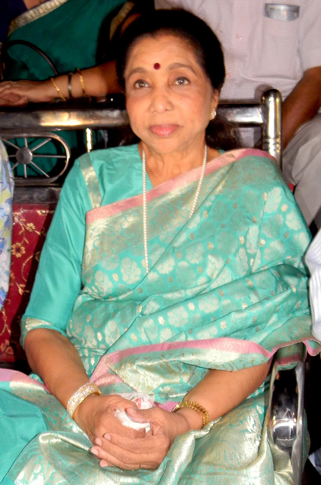 Asha Bhosle seated in a turquoise sari at Utkal Mandap, with the complete event frame retained