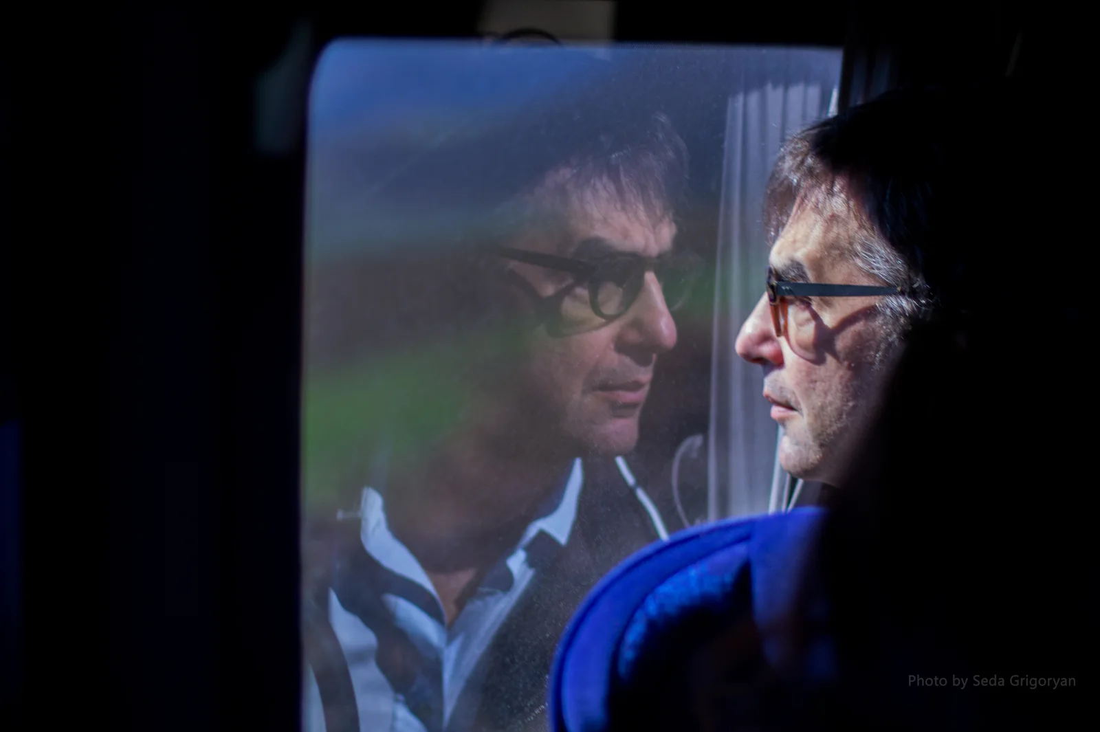 Atom Egoyan wearing glasses beside a window in Armenia in 2017, with his reflection and Seda Grigoryan’s photographer credit visible