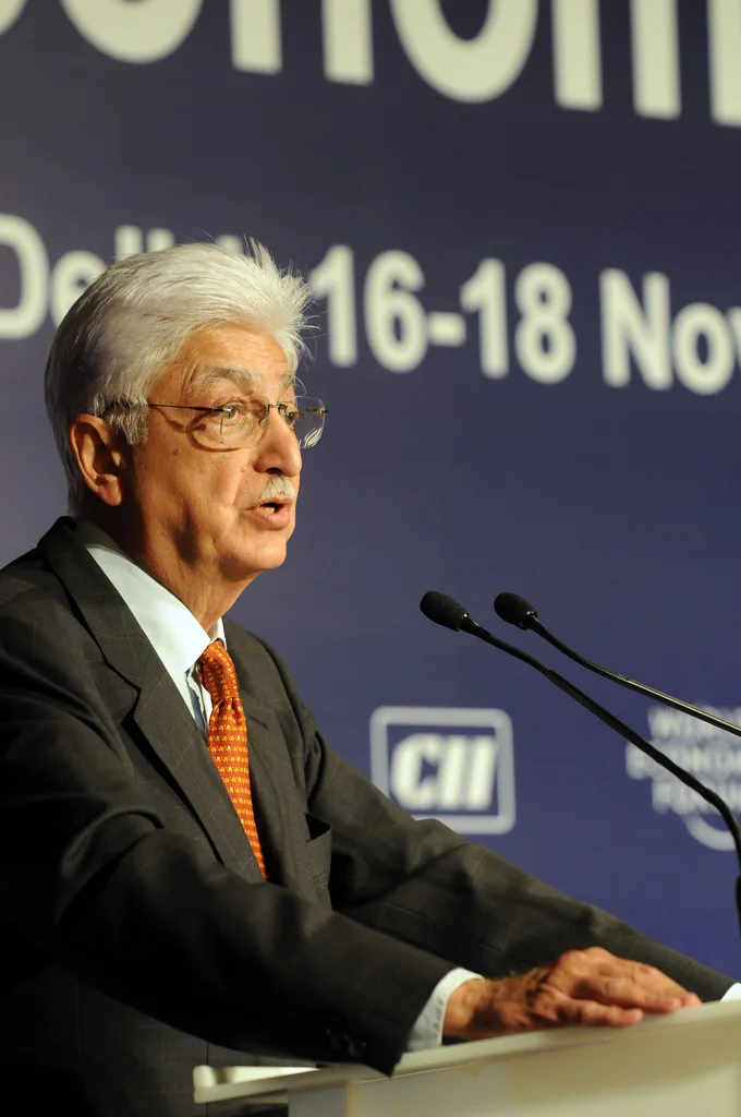 Azim Premji speaking at two microphones during the India Economic Summit in New Delhi in November 2008, with the complete forum backdrop and lectern.
