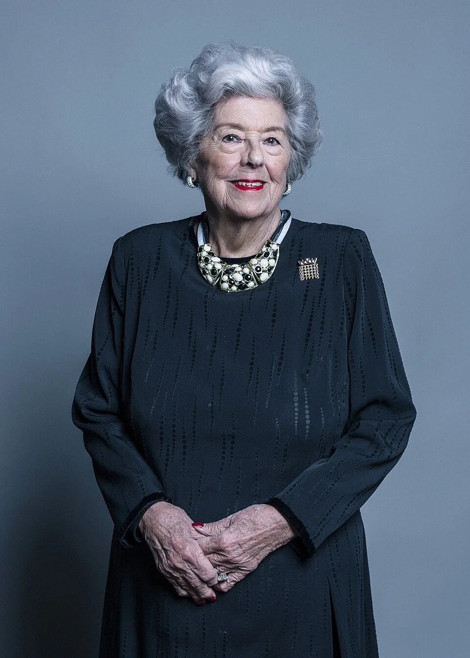 Betty Boothroyd standing in a blue dress with her hands together in her March 2018 parliamentary photograph; complete supplied frame retained.