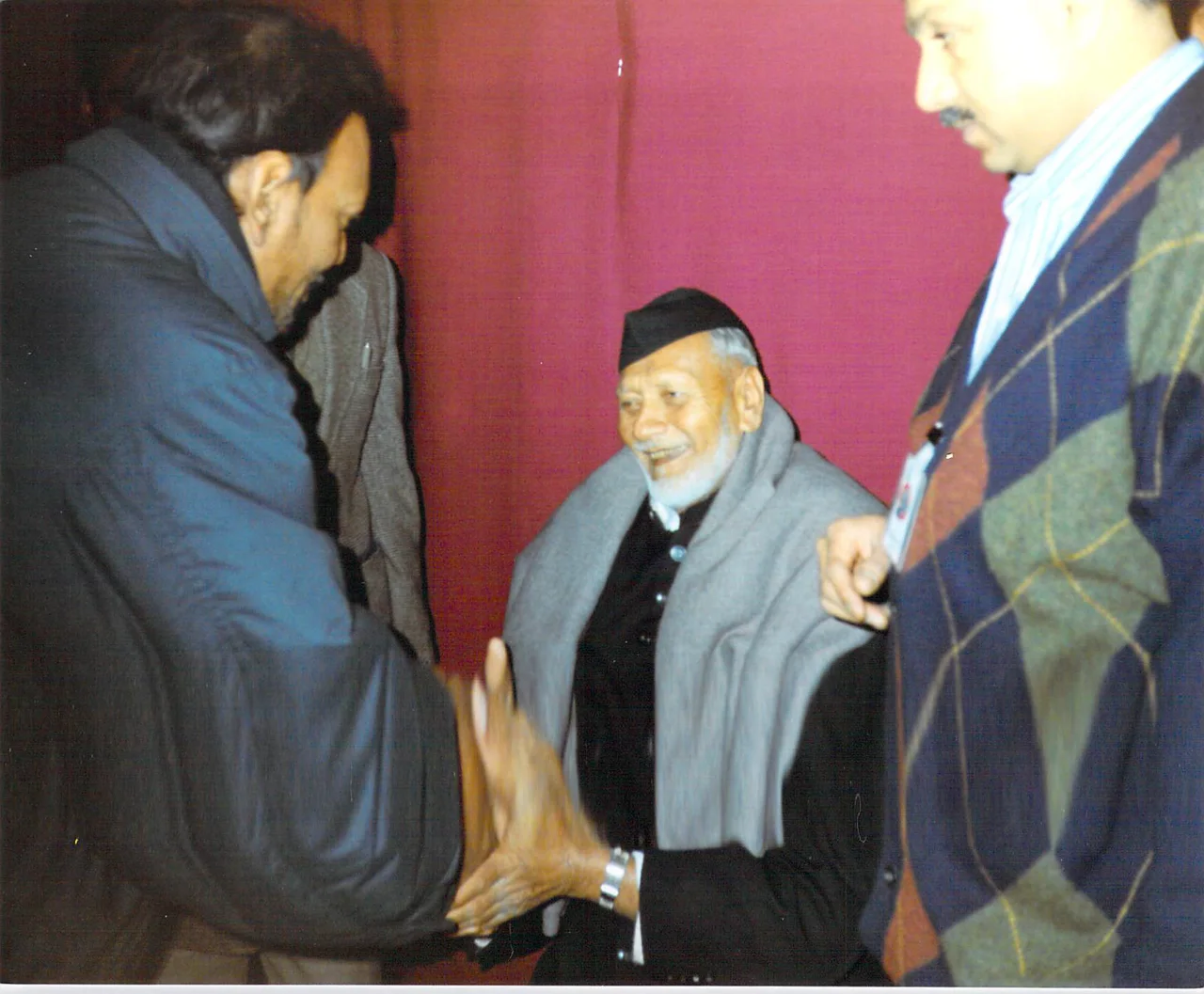 Bismillah Khan seated near the centre in a grey shawl, smiling among other people in Leicester in 1993