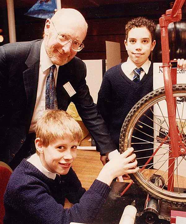 Clive Sinclair at left leaning towards two young inventors and their bicycle equipment in Bristol in 1992; complete supplied group photograph.