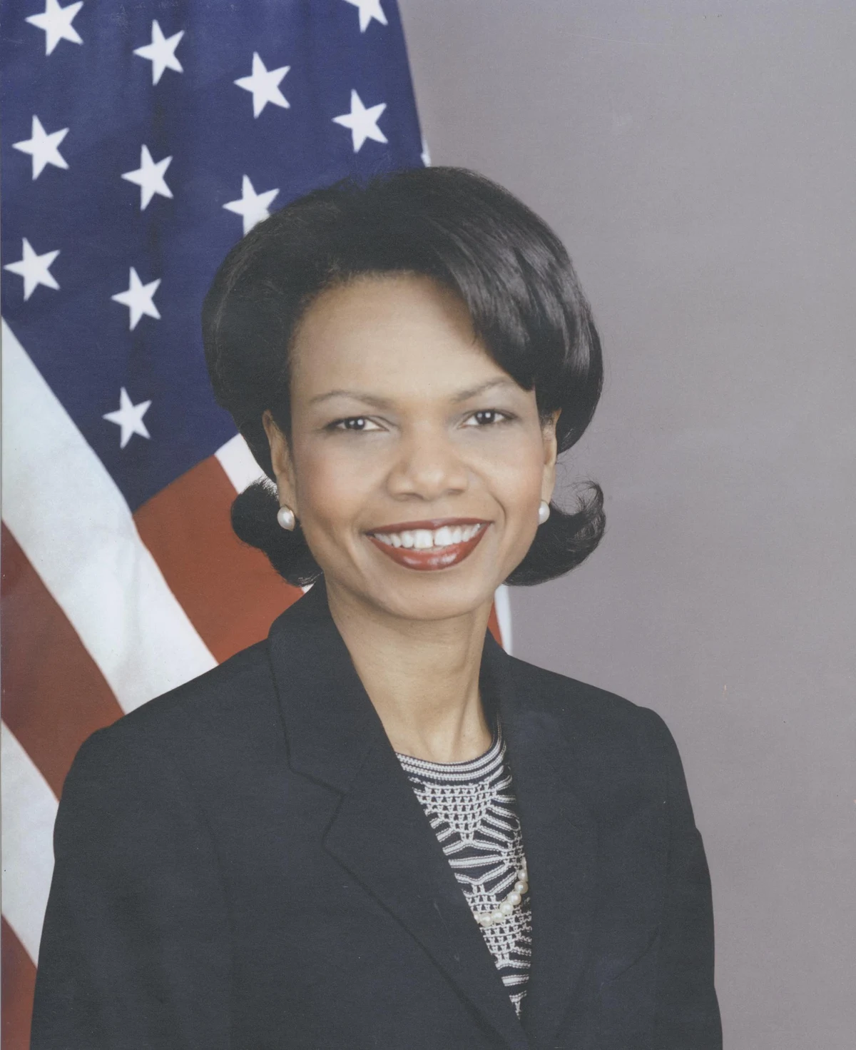 Condoleezza Rice’s full supplied State Department portrait with an American flag, dark jacket and patterned blouse, retaining its original pale contrast.