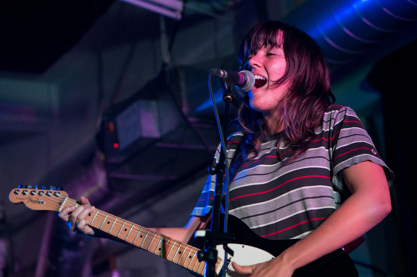 Courtney Barnett singing and playing guitar at Rough Trade East, London, with the complete microphone, guitar neck and stage background retained.