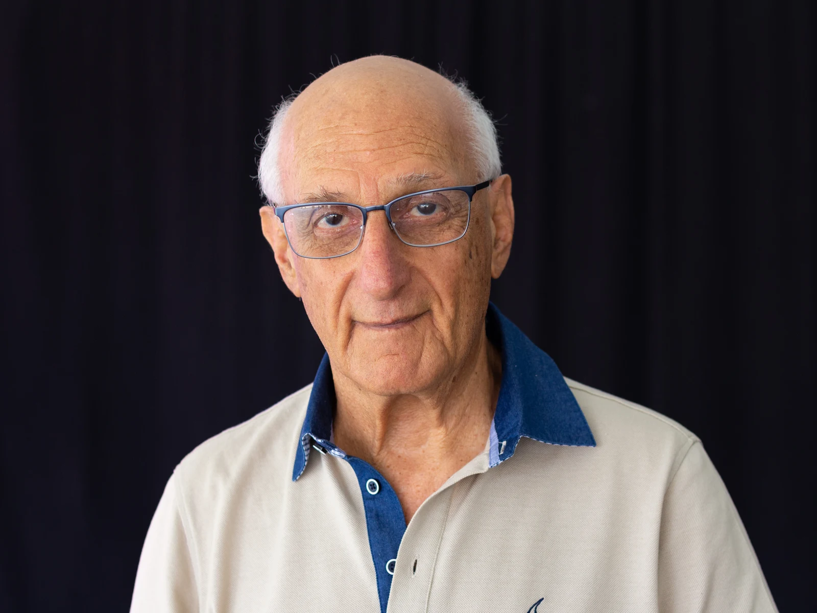 David Malouf wearing glasses and a light polo shirt against a dark background at Perth Writers Week in February 2019.