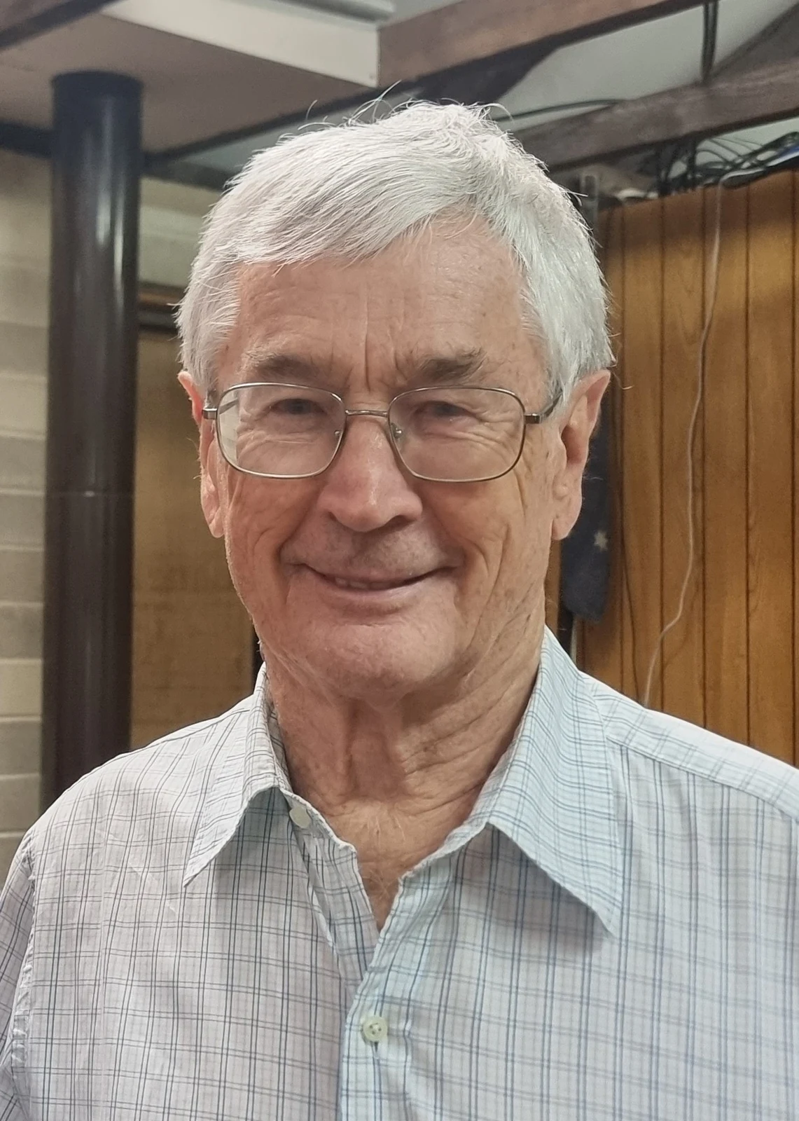 Dick Smith wearing glasses and a pale checked shirt at the Manly-Warringah Radio Society in 2023, with the full wooden interior framing retained.