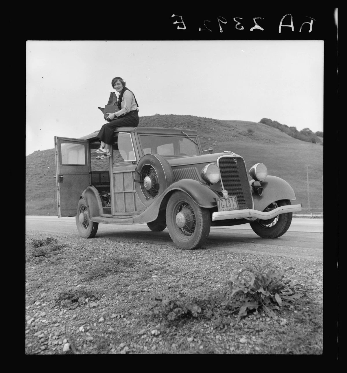 Dorothea Lange sitting on an automobile with a camera in California in February 1936, shown within the full original negative scan and its edge markings