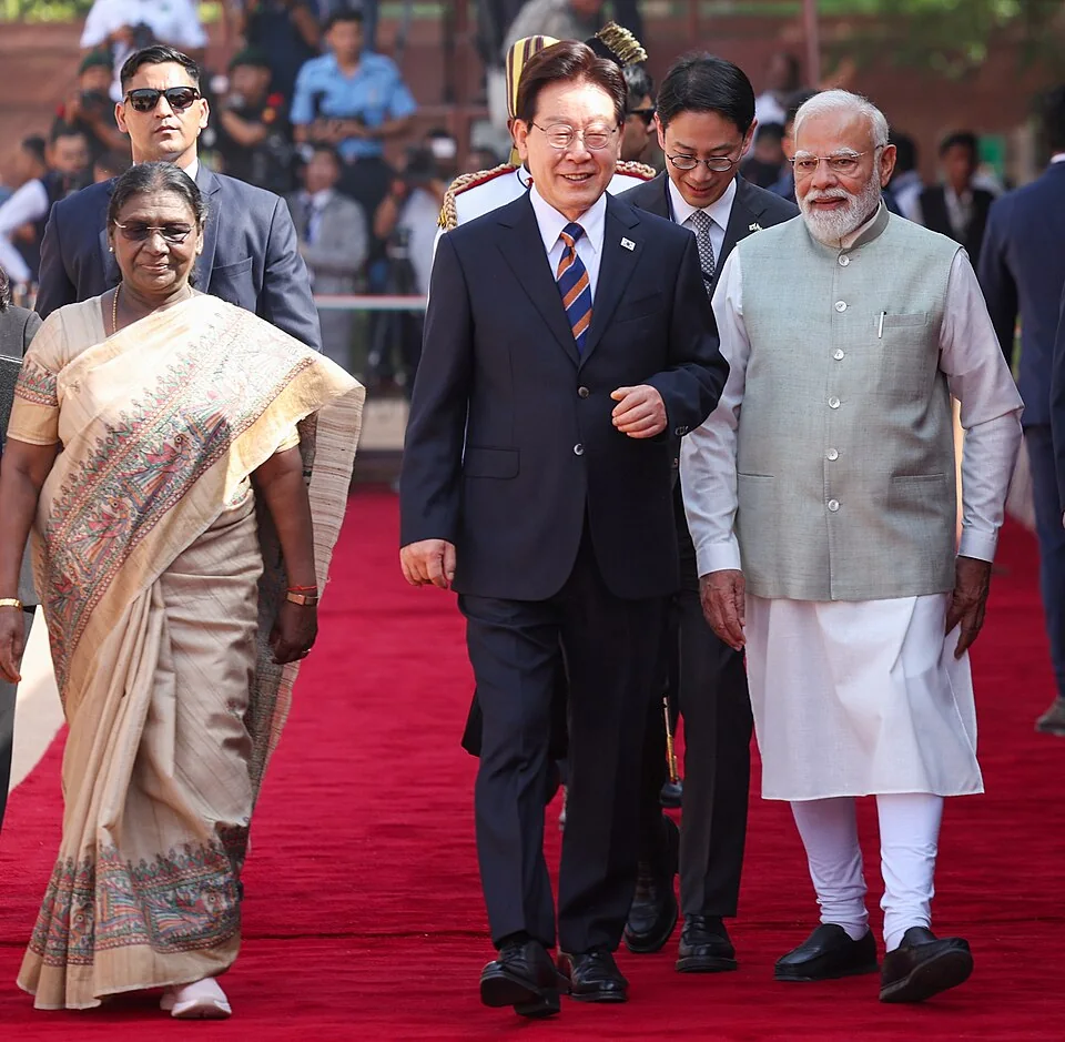 Droupadi Murmu at left walks with South Korean president Lee Jae-myung at centre and Narendra Modi at right in April 2026, with attendants behind them.