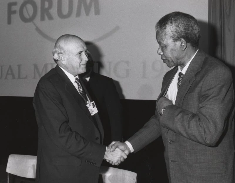 F. W. de Klerk at left shaking hands with Nelson Mandela at Davos in January 1992, retaining the entire historical black-and-white frame.