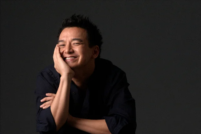 Glen Goei smiling in a seated studio portrait supplied by TigerTiger Productions.