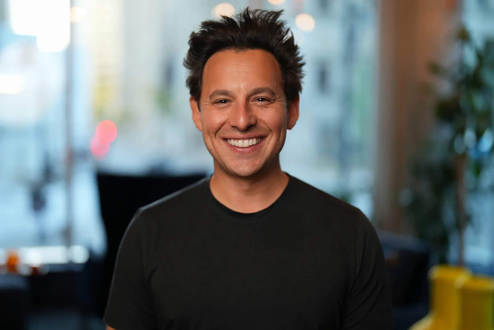 Harley Finkelstein smiles towards the camera wearing a black T-shirt against a softly focused office background, in Seibeltron’s complete supplied photograph.