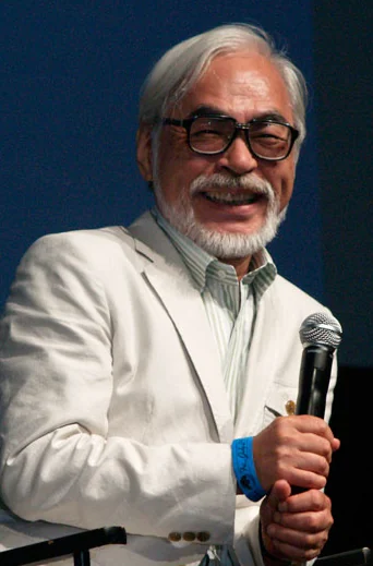 Hayao Miyazaki smiling and holding a microphone at San Diego Comic-Con in 2009.