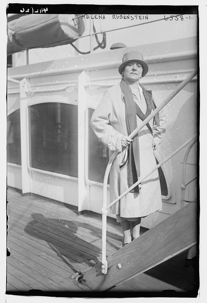 Complete black-and-white Bain News Service photograph of Helena Rubinstein standing beside shipboard steps, preserving the negative border and handwritten Helena Rubenstein inscription.
