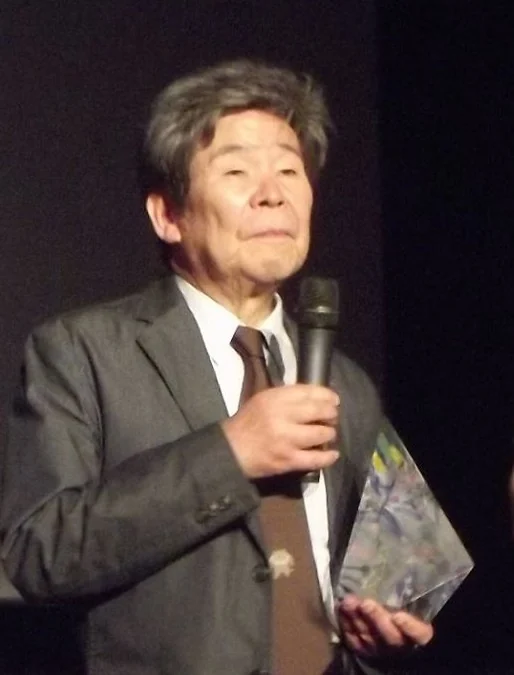 Isao Takahata at Annecy in 2014, holding a microphone and an award, in the full supplied vertical frame.
