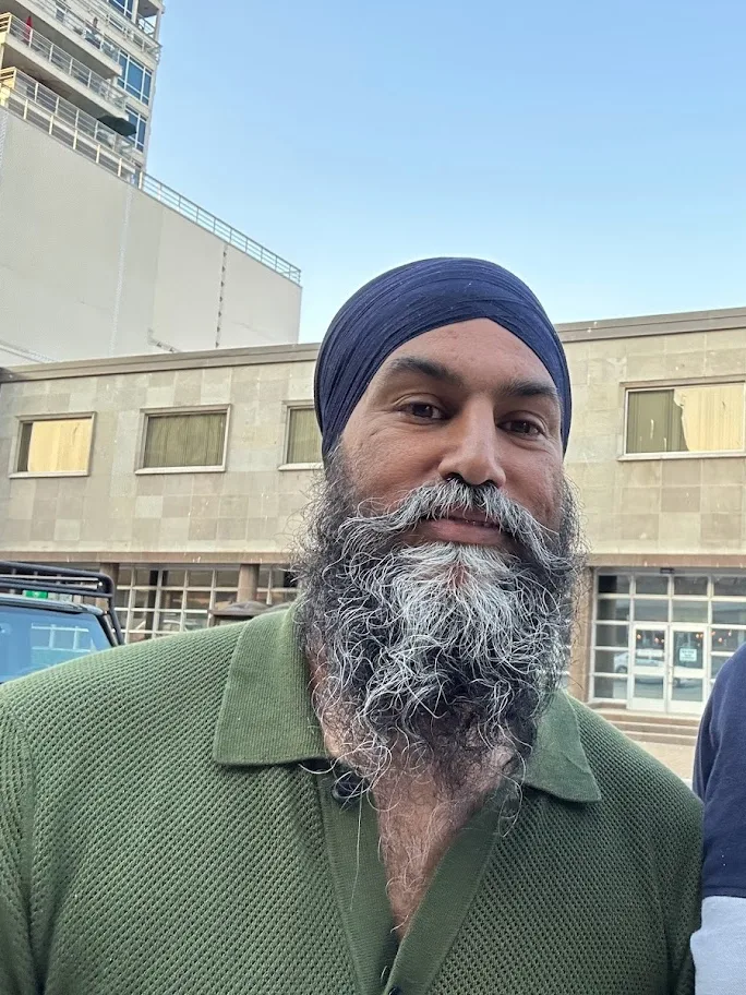 Jagmeet Singh in a navy turban and green shirt in Nanaimo on 27 August 2023; the full supplied image includes the surrounding buildings and part of another person at the right edge.
