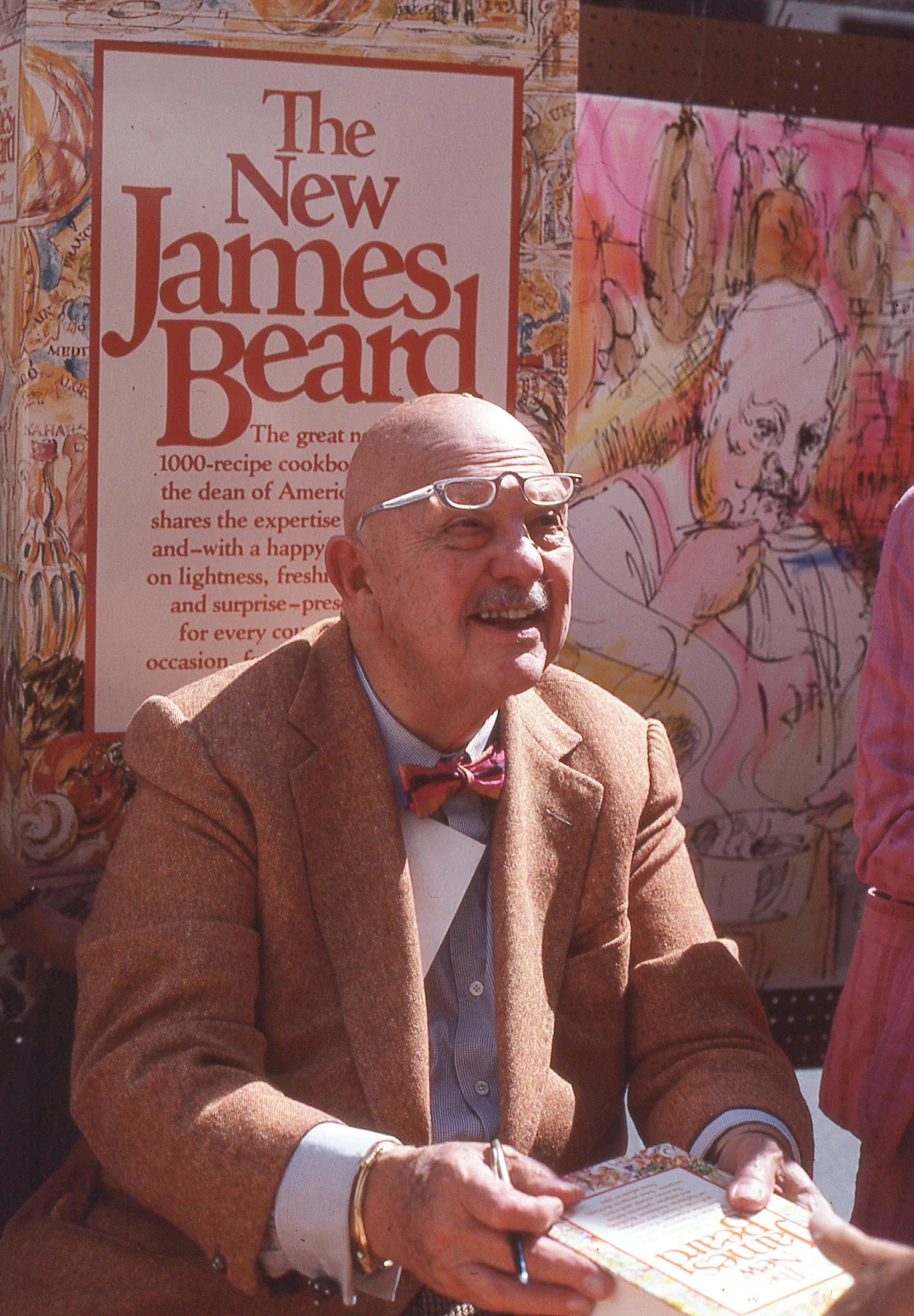 James Beard signing a cookbook in Bill Golladay's color photograph dated 20 September 1981, with the complete supplied frame and surrounding book display retained.