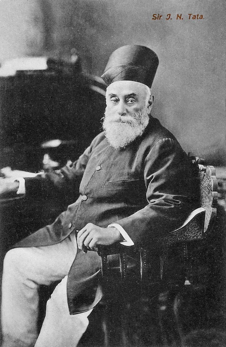 Jamsetji Tata seated in a patterned armchair wearing a Parsi cap, in a complete monochrome postcard bearing the printed caption Sir J. N. Tata.