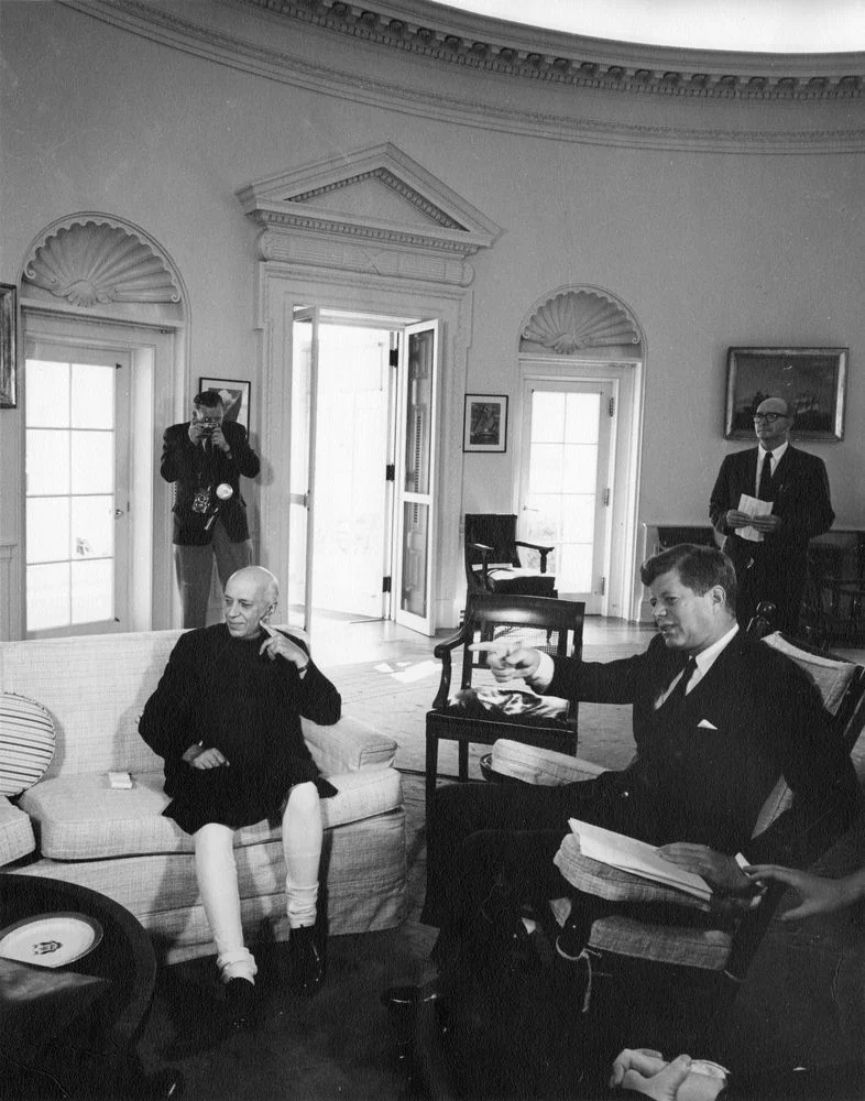 Jawaharlal Nehru seated at left and John F. Kennedy seated at right in the Oval Office in 1961, with two men standing behind them.