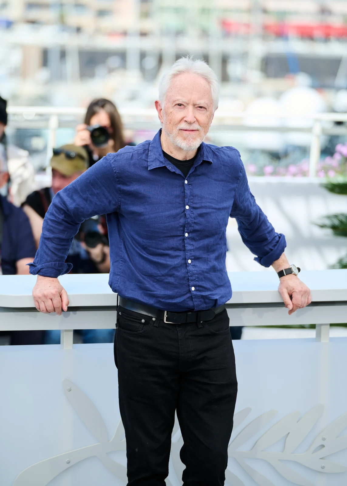 J. M. Coetzee at a 2026 Cannes photocall in a blue shirt, with the complete published portrait, railing and background photographers retained.