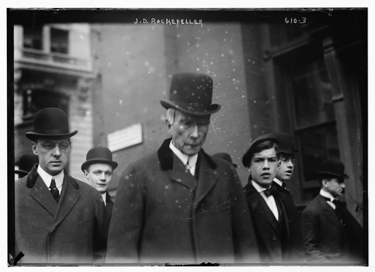 John D. Rockefeller at the center of a complete Bain News Service street photograph in New York, with the original negative borders and handwritten caption visible