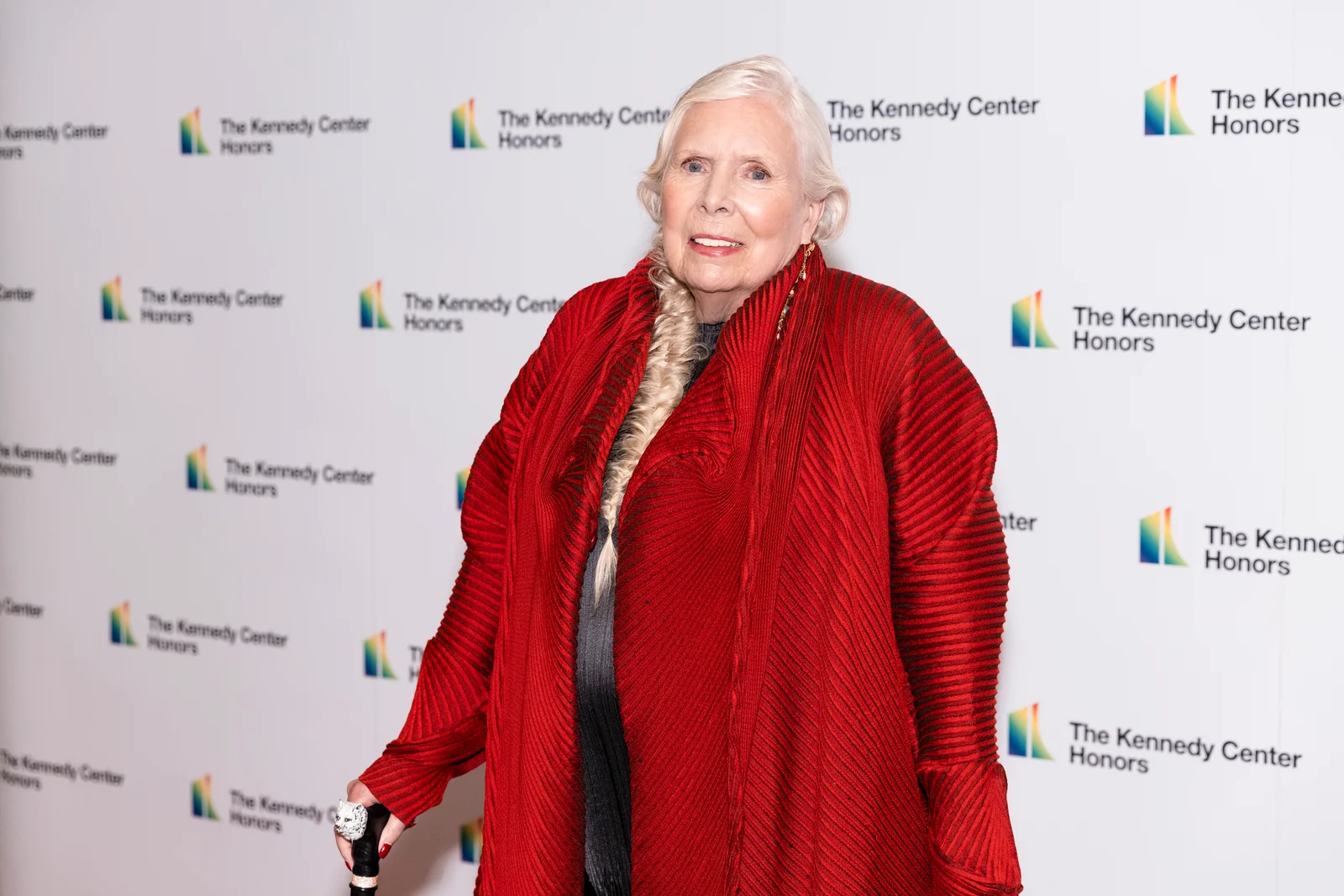 Joni Mitchell wearing a red wrap and holding a cane at a 2021 honours ceremony