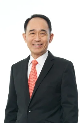 Kan Trakulhoon wearing a dark suit and red tie in a standing portrait.