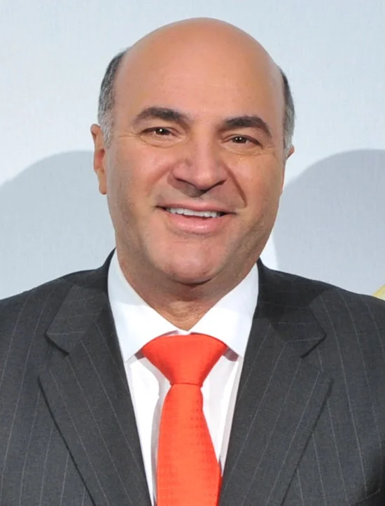 Kevin O’Leary smiling in a dark suit and red tie in the complete supplied May 2012 portrait, without enlargement.