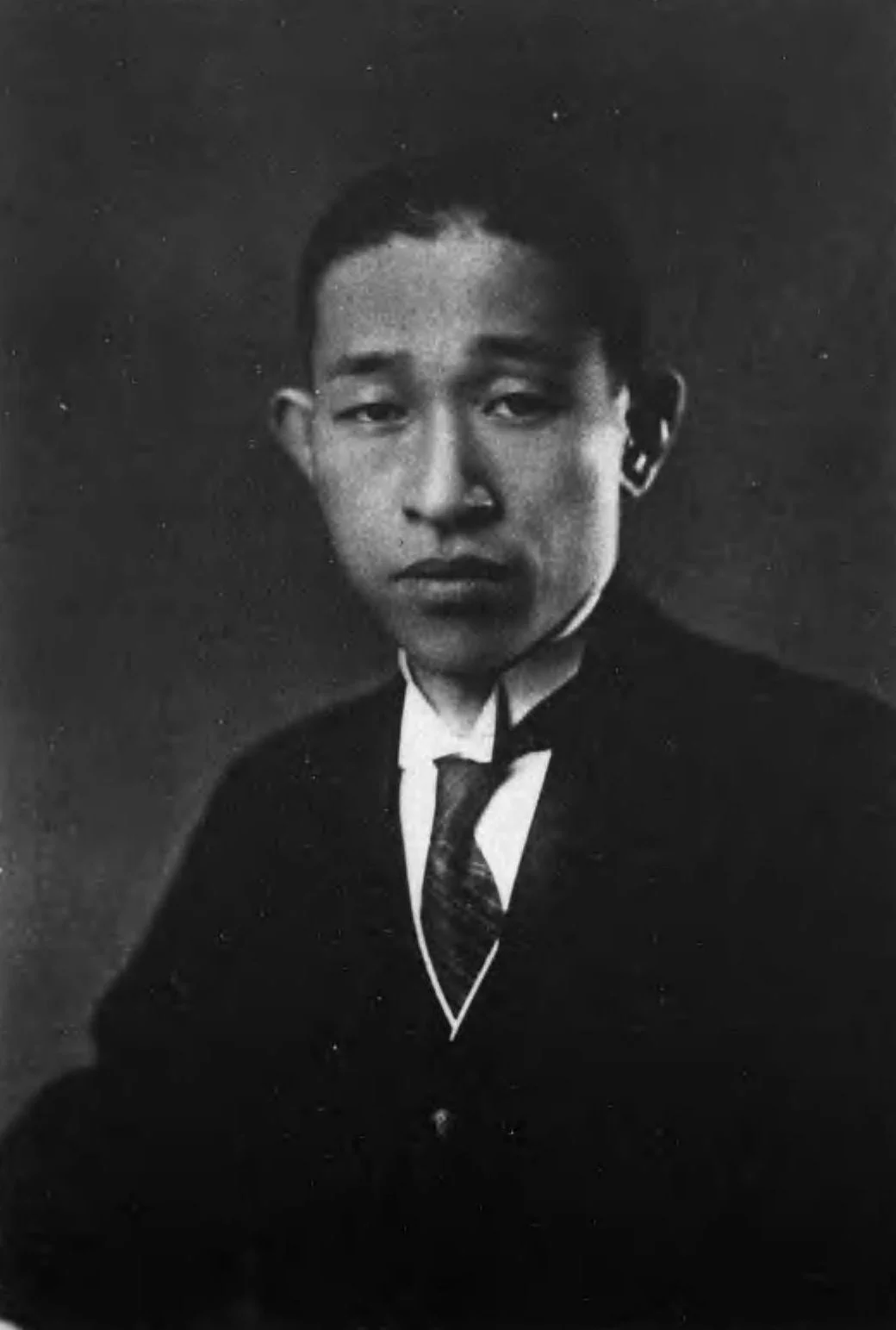 Historical black-and-white portrait of a young Konosuke Matsushita in a suit.