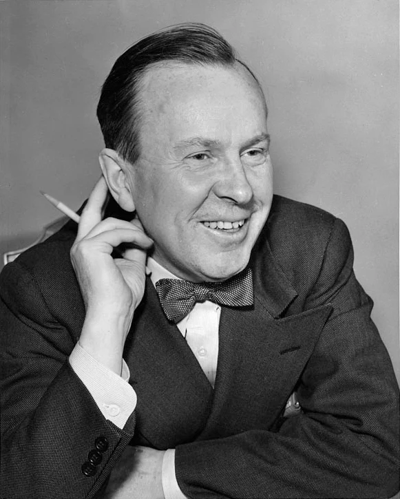Lester B. Pearson smiles while seated with a pencil held near his ear, wearing a dark jacket and patterned bow tie in a 1944 photograph.
