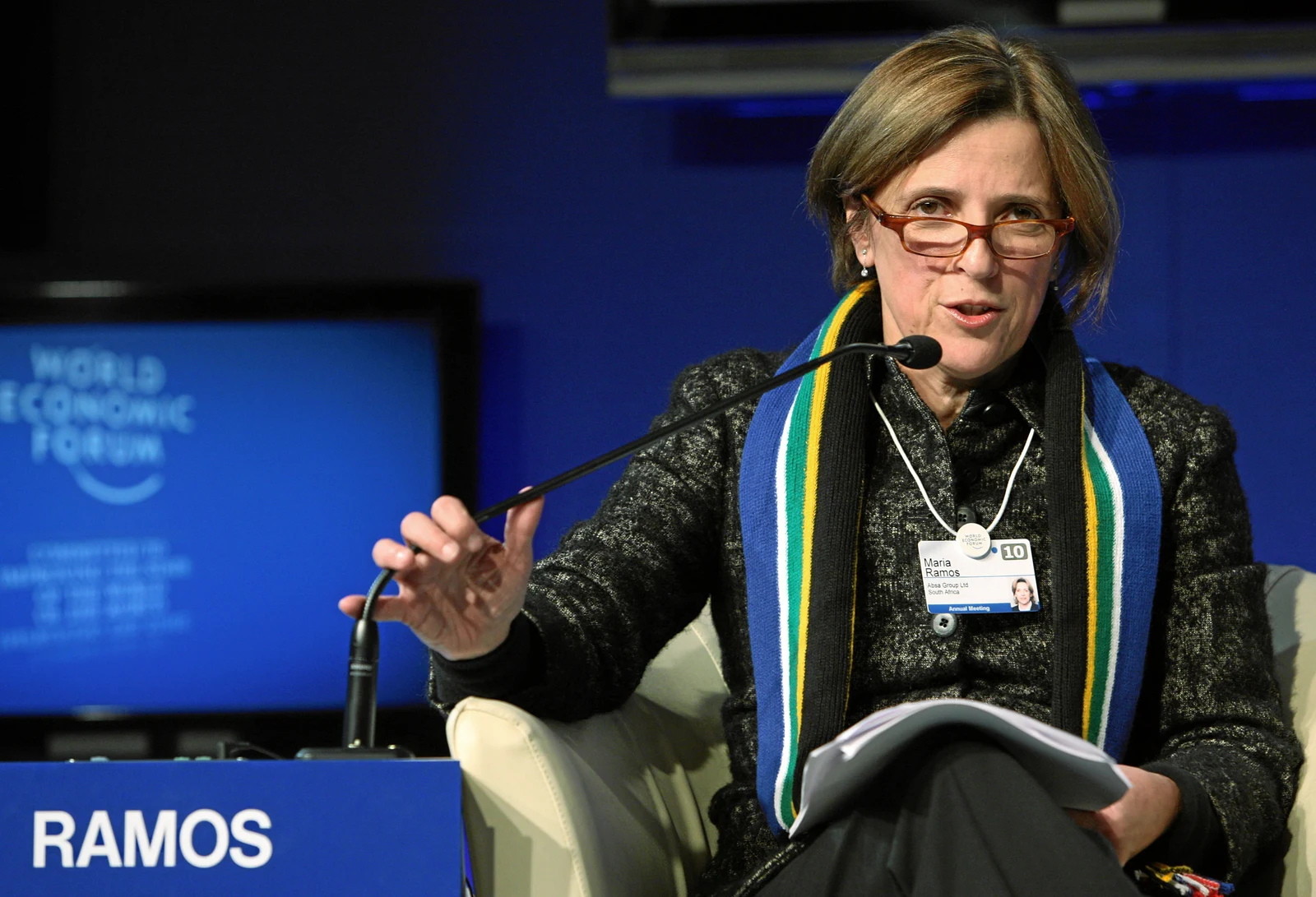 Maria Ramos speaking at Davos in the complete 2010 horizontal photograph, with nameplate, raised hand, papers, chair and event background retained.