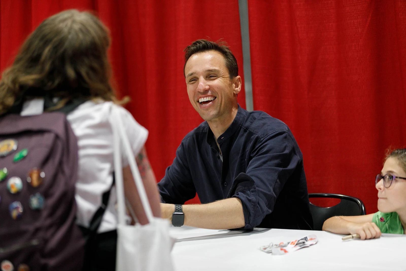 Markus Zusak smiling at a 2019 National Book Festival signing table, with attending readers and the entire supplied frame retained.
