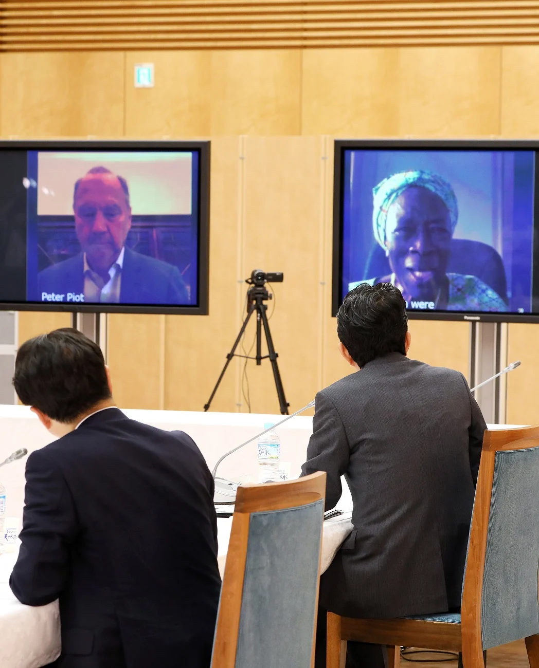 Miriam Were appears on the right video screen and Peter Piot on the left at the2020Noguchi Prize meeting;complete supplied Cabinet Secretariat photograph.