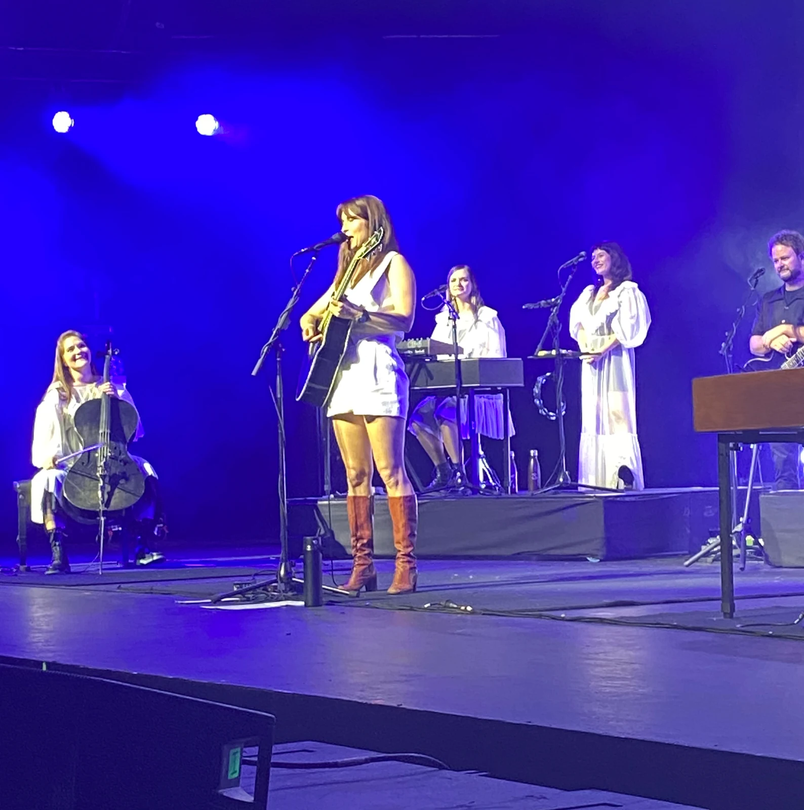 Missy Higgins at the front of a blue-lit Melbourne stage with guitar and fellow performers during the December 2024 Second Act tour; complete supplied frame