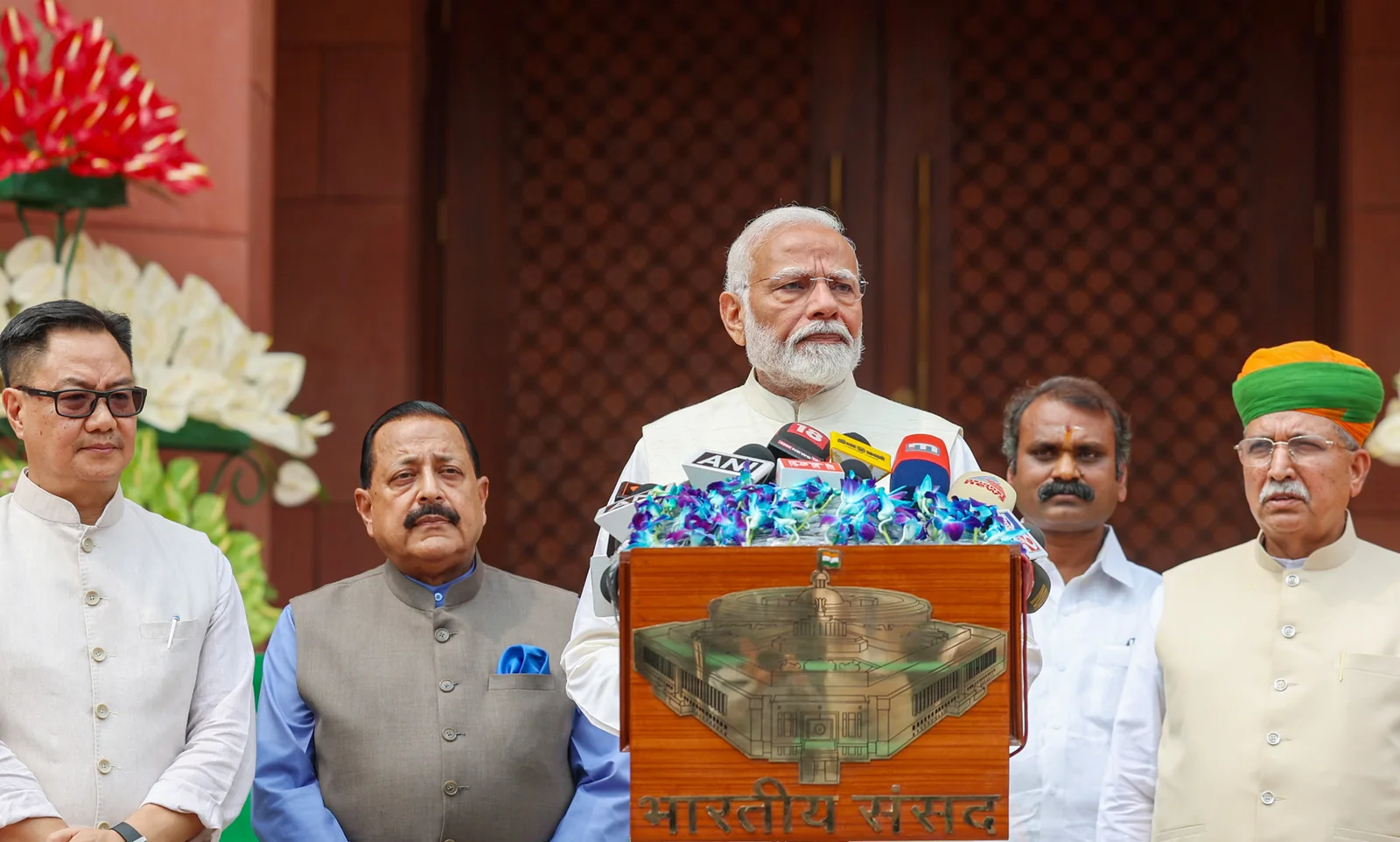Narendra Modi speaks behind microphones outside Parliament in June 2024, with three ministers standing beside him.
