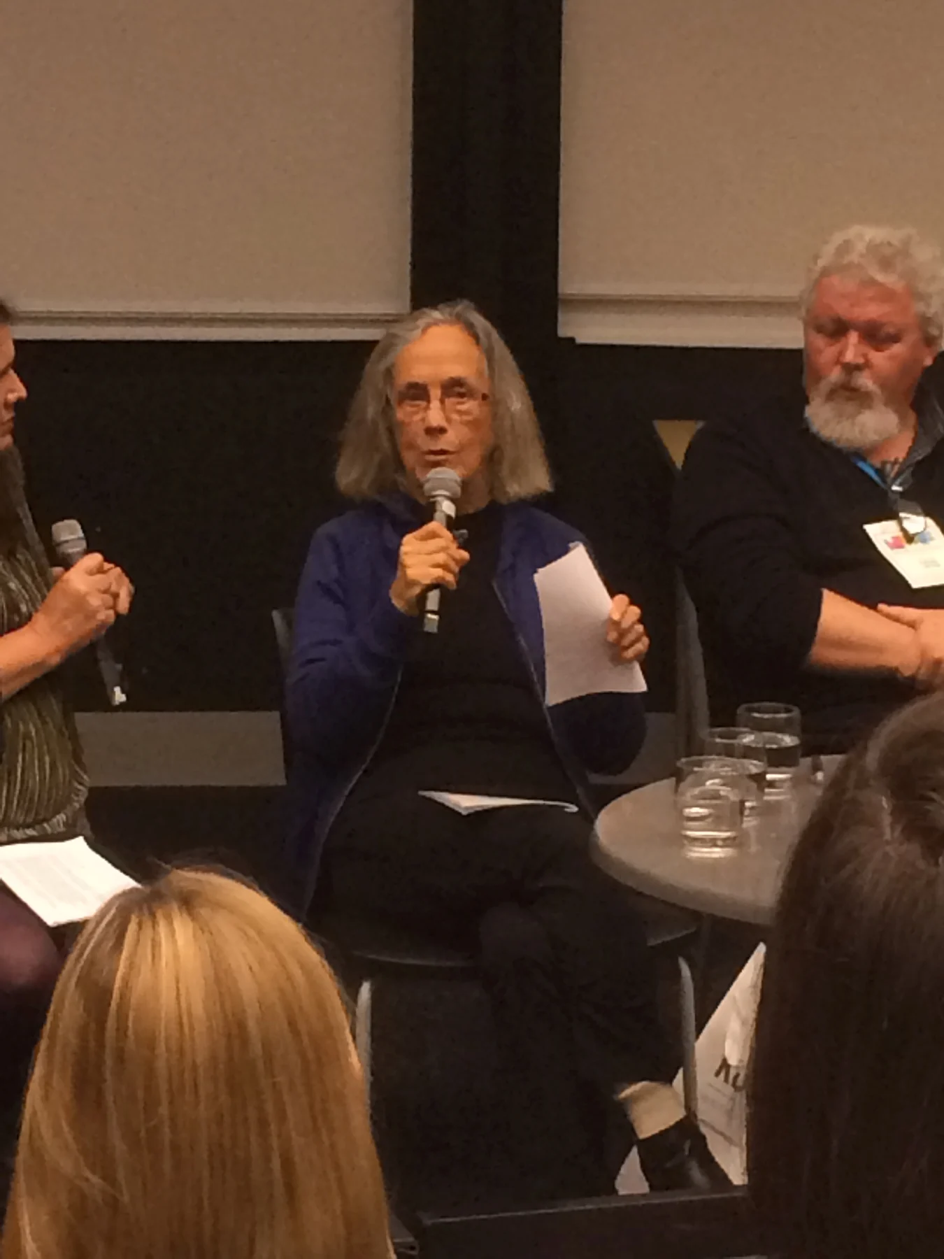 Patricia Grace speaking into a microphone at the National Writers Forum, with other panellists and audience retained.