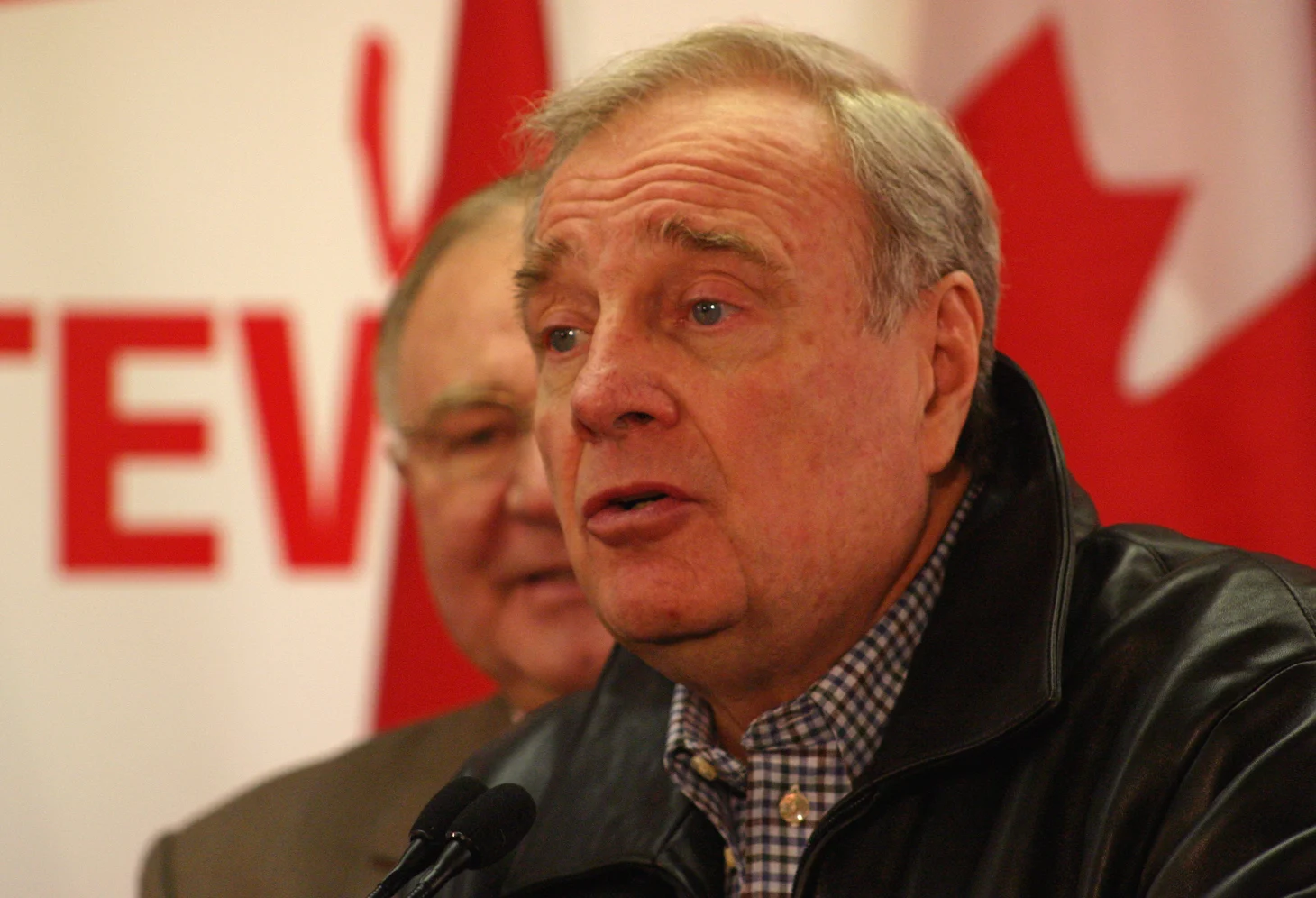 Paul Martin in the foreground speaking at microphones in 2006, with another person behind him