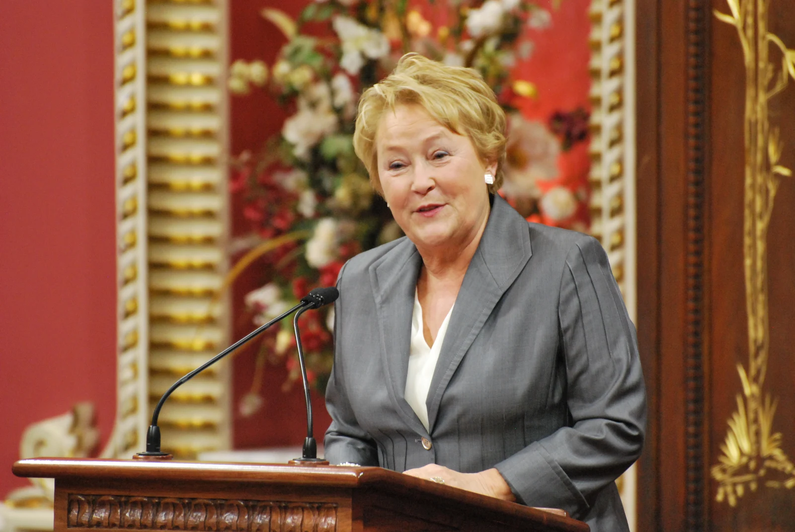 Pauline Marois speaking at a lectern in the red and gold room used for the 2013 Ordre national du Québec ceremony