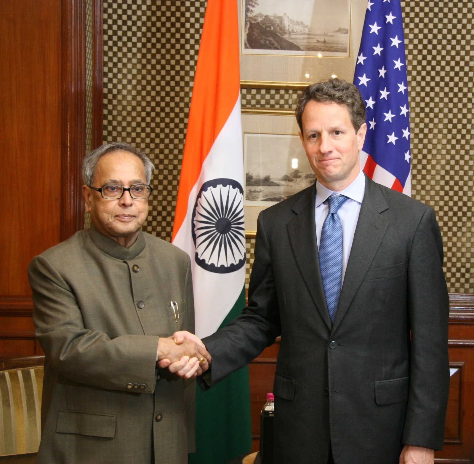 Pranab Mukherjee at left shakes hands with Timothy Geithner at right in New Delhi in April 2010; both national flags and the complete room setting remain visible.