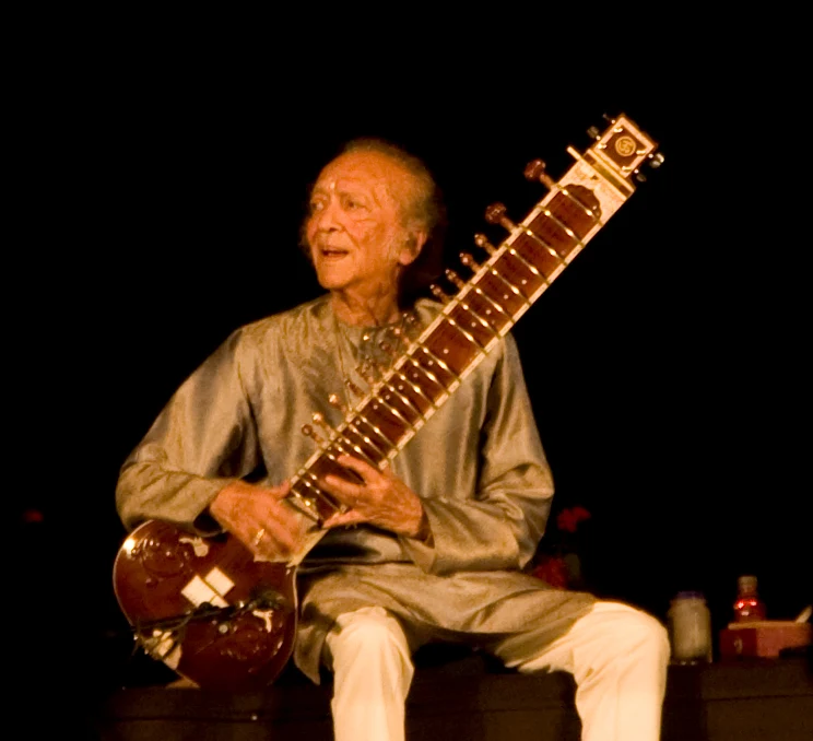 Alexandra Ignatenko’s complete 2009 Delhi photograph of Ravi Shankar seated with his sitar, retaining the dark stage and objects at the right edge