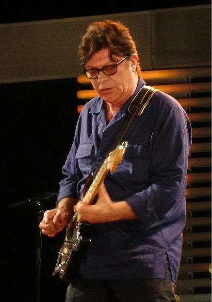 Robbie Robertson wearing glasses and a navy shirt while playing guitar at the 2007 Crossroads Guitar Festival, with the complete supplied border retained