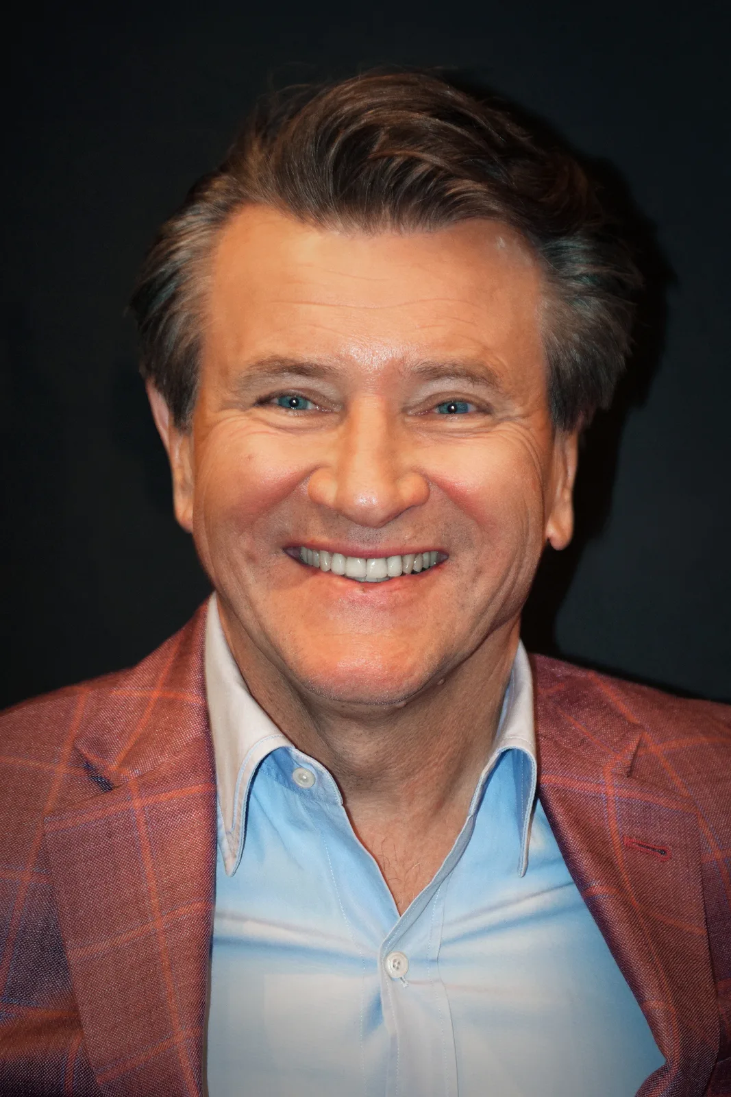 Robert Herjavec smiles in a red checked jacket and pale blue shirt at PaleyFest 2023, in Philip Romano’s complete supplied portrait frame.