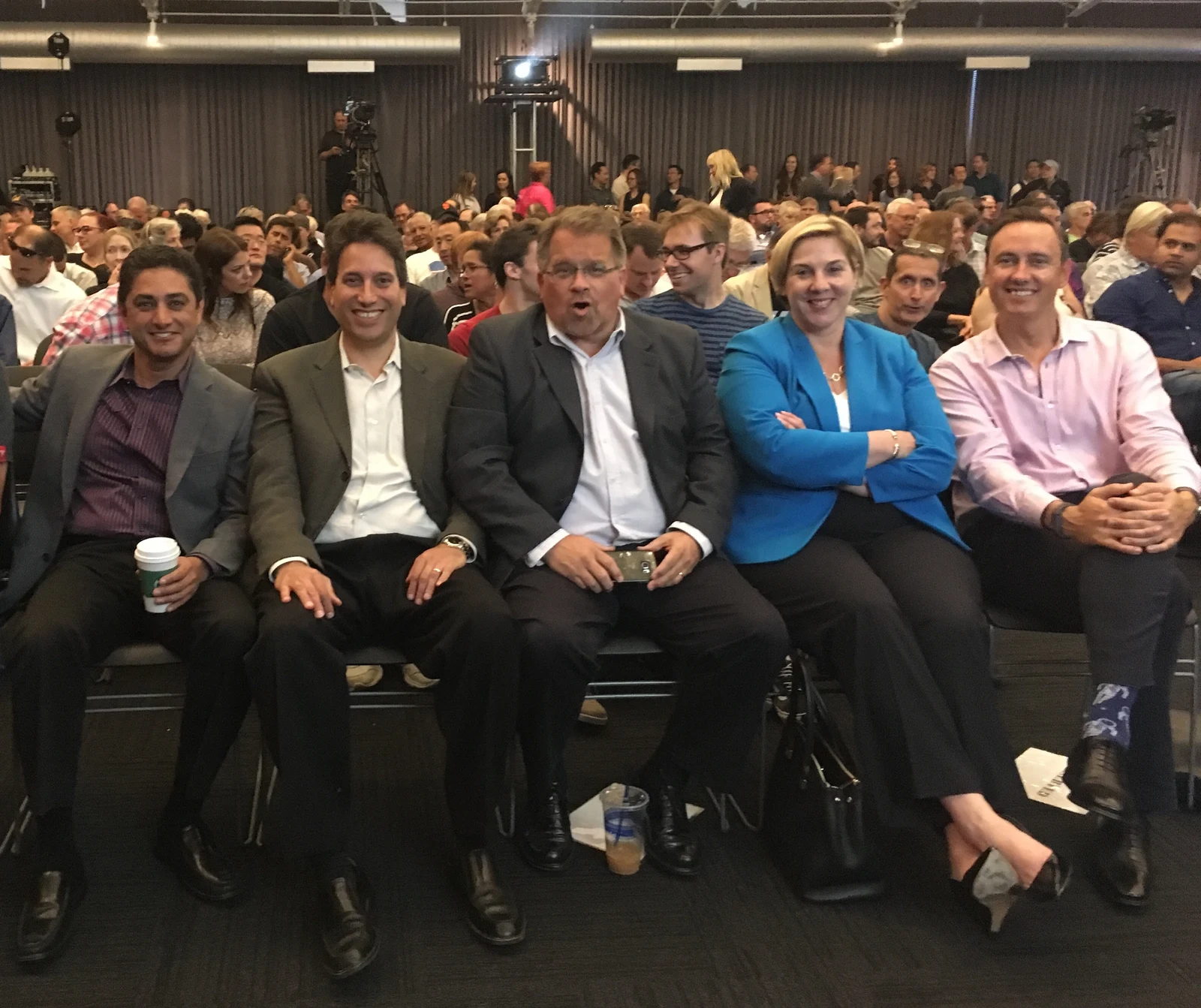 Full Tesla shareholder-meeting audience photograph: Robyn Denholm in a blue jacket is fourth from left among five directors in the front row, with the surrounding people and room retained.