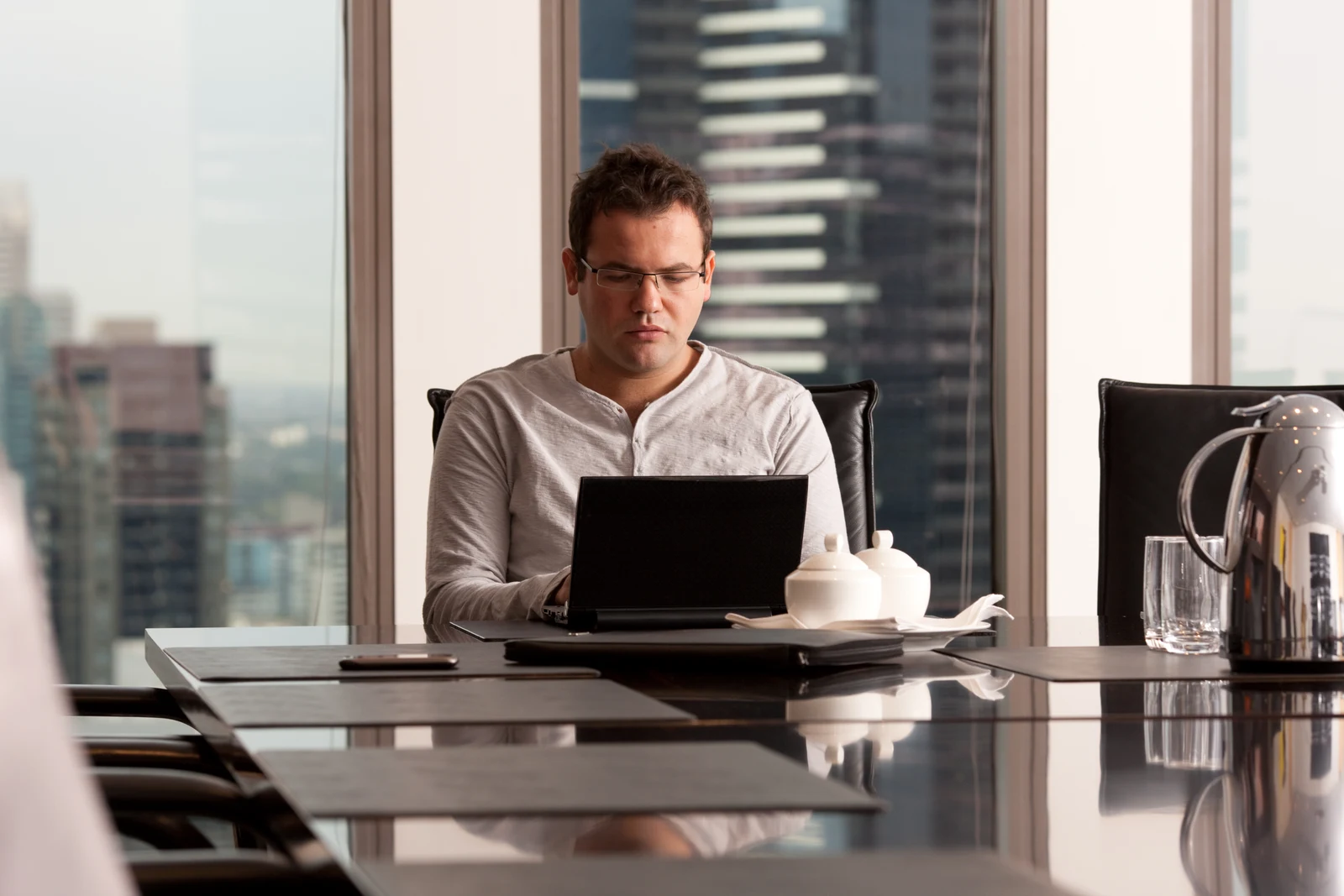 Ruslan Kogan working at a laptop at a conference table in 2010, with the complete windows, empty chair, tableware and surrounding supplied frame retained.
