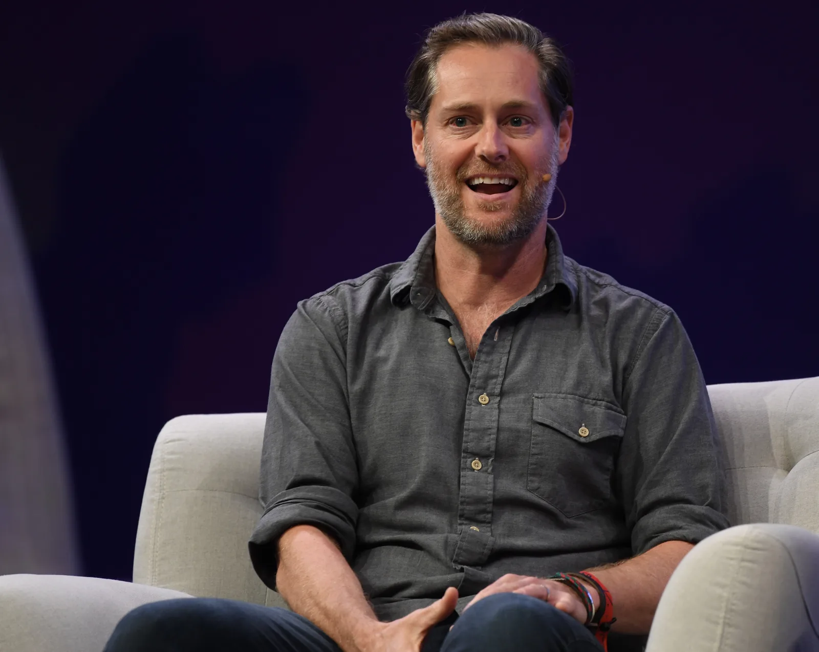 Ryan Holmes sits on a pale chair wearing a grey shirt and headset microphone at Collision in Toronto in May 2019, in the complete supplied frame.