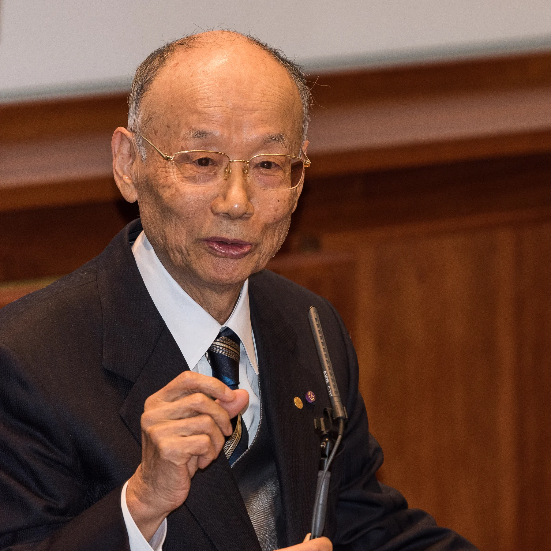 Satoshi Ōmura speaking into a microphone in Stockholm, with the complete supplied photograph retained.