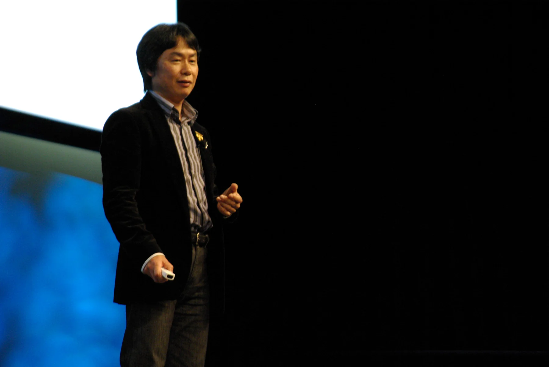 Shigeru Miyamoto standing at GDC 2007 with a Wii Remote, surrounded by the full stage and projection-screen frame.